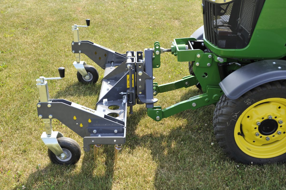 Nahaufnahme eines Matev Rasenstriegels SCA 130, montiert an einem John Deere 2036R Traktor. Die robusten Räder und die Höhenverstellung sind deutlich sichtbar, platziert auf einer trockenen Rasenfläche.