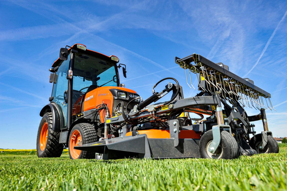 Ein Kubota STW40 Traktor mit einem Frontmäher im Einsatz auf einer grünen Wiese unter einem klaren blauen Himmel, ausgestattet mit einem Matev Mähwerk für präzise und effiziente Grünflächenpflege.