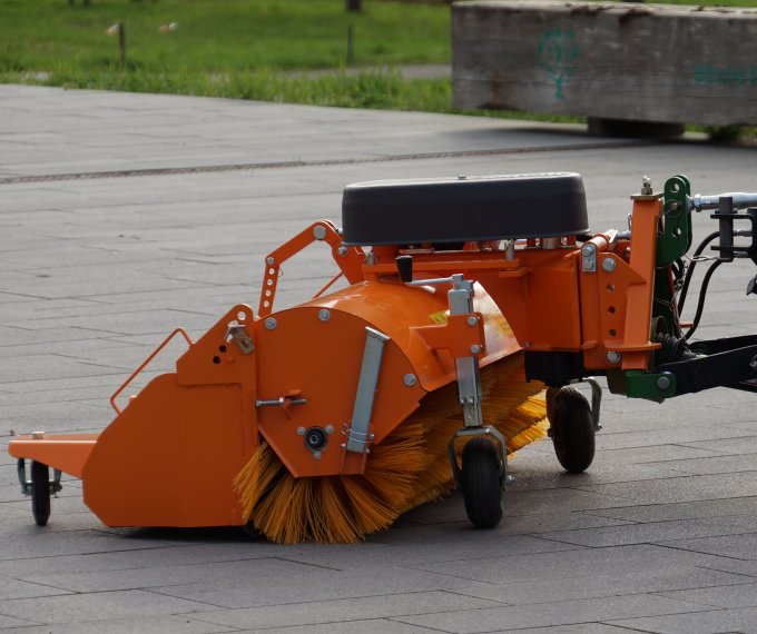 John Deere 2036R Traktor mit matev Kehrmaschine in Orange, ideal für die Reinigung von gepflasterten Flächen. Nahaufnahme der robusten Bürste und des Anbausystems, perfekt für professionelle Außenreinigung.