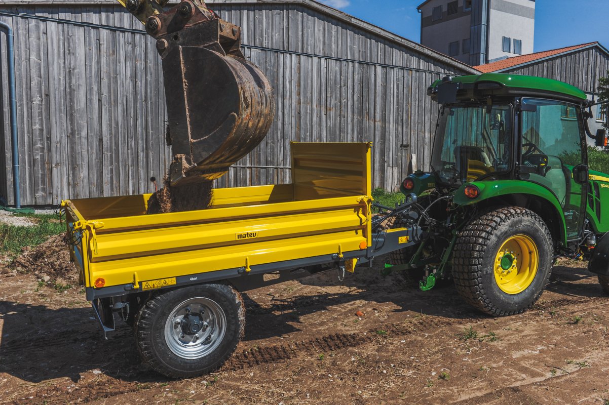 Tranktoranhänger Einachs-Dreiseitenkipper in der Farbe gelb für Traktoren in der Kommunaltechnik. Dieser wird gerade beladen.