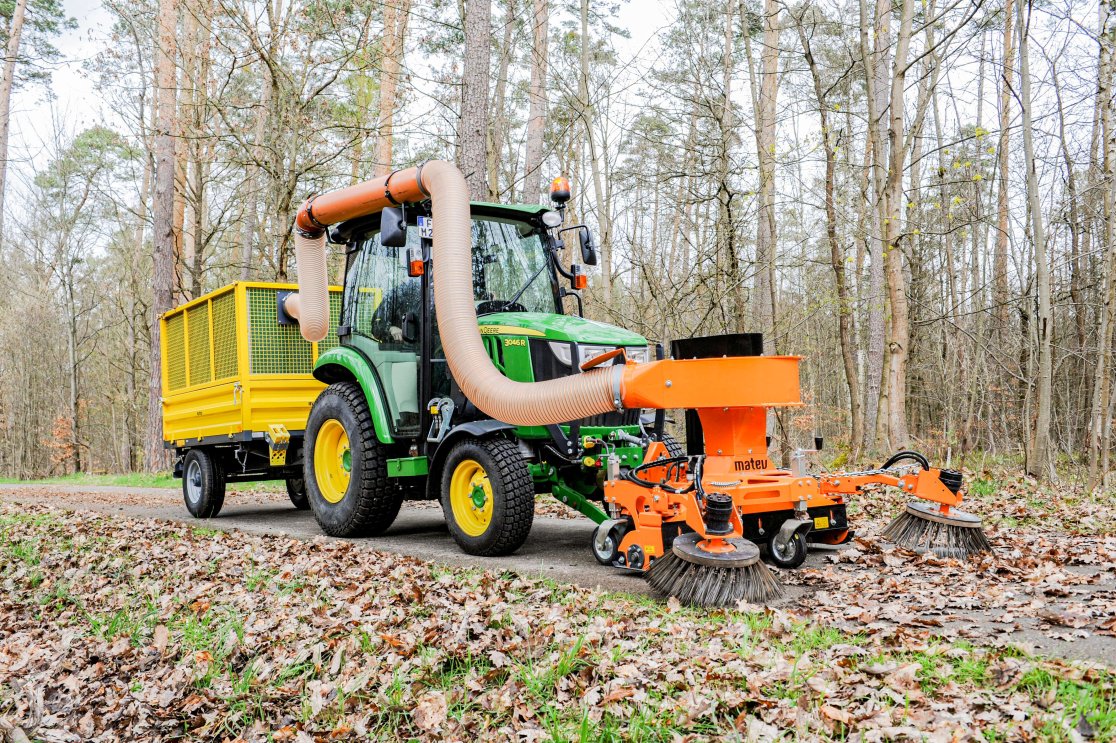 Ein Anbaugerät Saugkehrmaschine im Einsatz an einem John Deere 2026r Traktor im Wald zur Flächenpflege und im kommunalen Einsatz.
